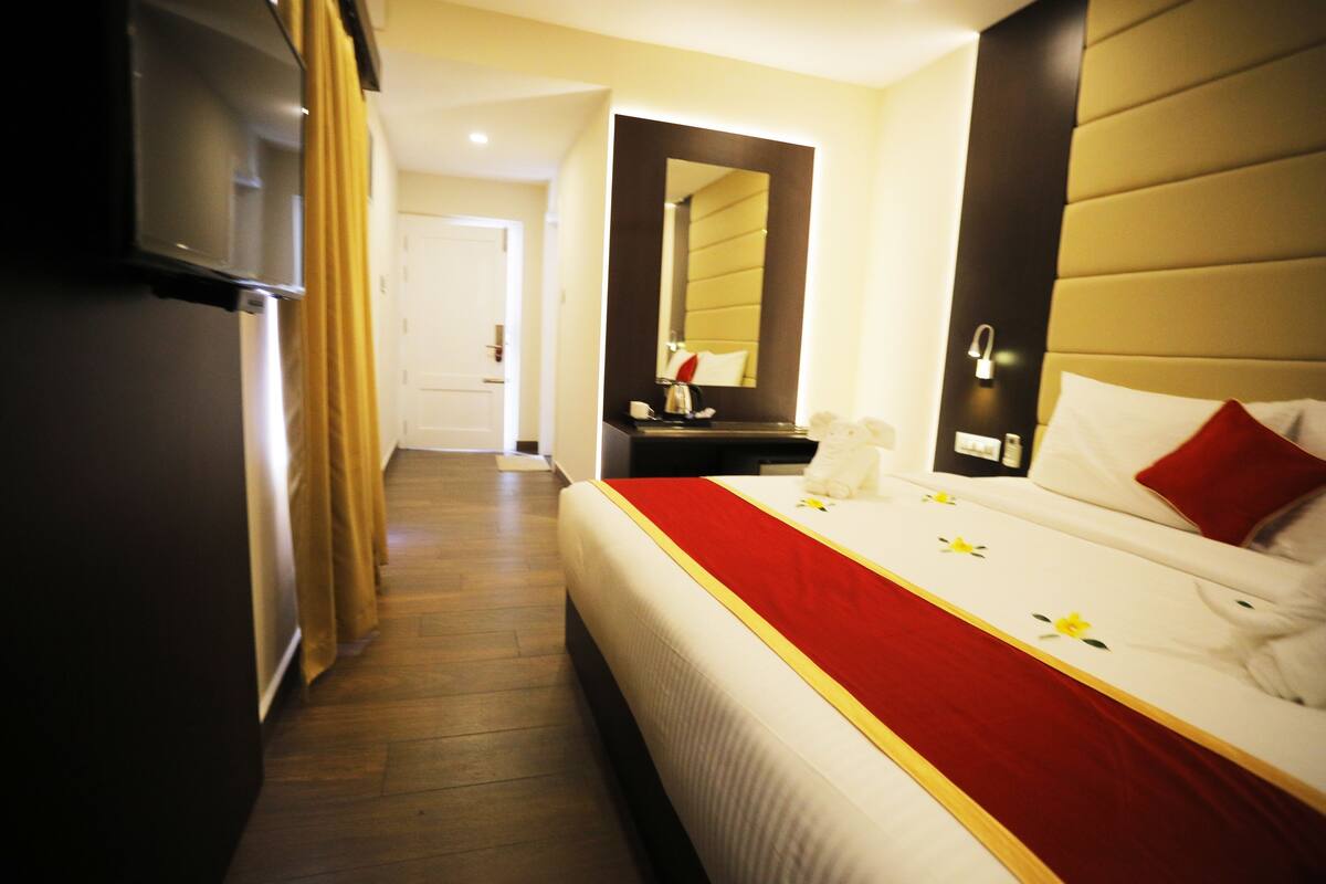 A hotel room with a bed, a bedside table, a mirror, and a door leading to another room.