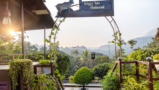 Señal de restaurante Nilgiri Tahr con una escultura de cabra, rodeada de abundante vegetación y un paisaje montañoso.