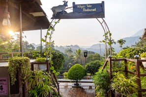 Señal de restaurante Nilgiri Tahr con una escultura de cabra, rodeada de abundante vegetación y un paisaje montañoso.