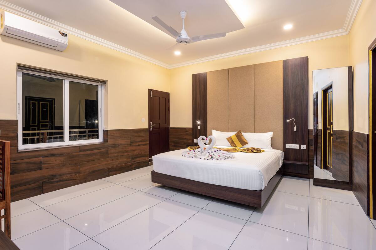 A modern hotel room with a large bed, a ceiling fan, a window with a view, and a wardrobe with a mirror.