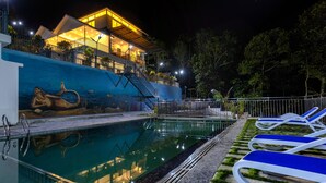 Una piscina con un mural, sillas de descanso y una escalera que lleva a un edificio.