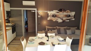 Ett modernt kök med inbyggda vitvaror, en matplats med ett bord för två och en soffa i bakgrunden.