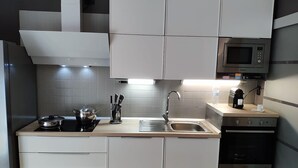 Ett modernt kök med vita skåp, en diskho i rostfritt stål, en mikrovågsugn och en kaffebryggare.