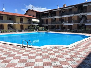 A swimming pool with a checkered tiled deck, surrounded by multi-story buildings with balconies. - Superb apartment in the center of Moniga with WIFI (Moniga del Garda)