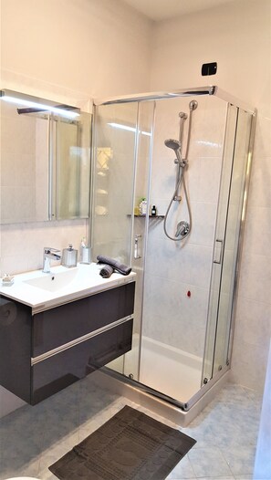 A modern bathroom with a glass-enclosed shower, a vanity with a mirror, and a small shelf with toiletries. - Superb apartment in the center of Moniga with WIFI (Moniga del Garda)