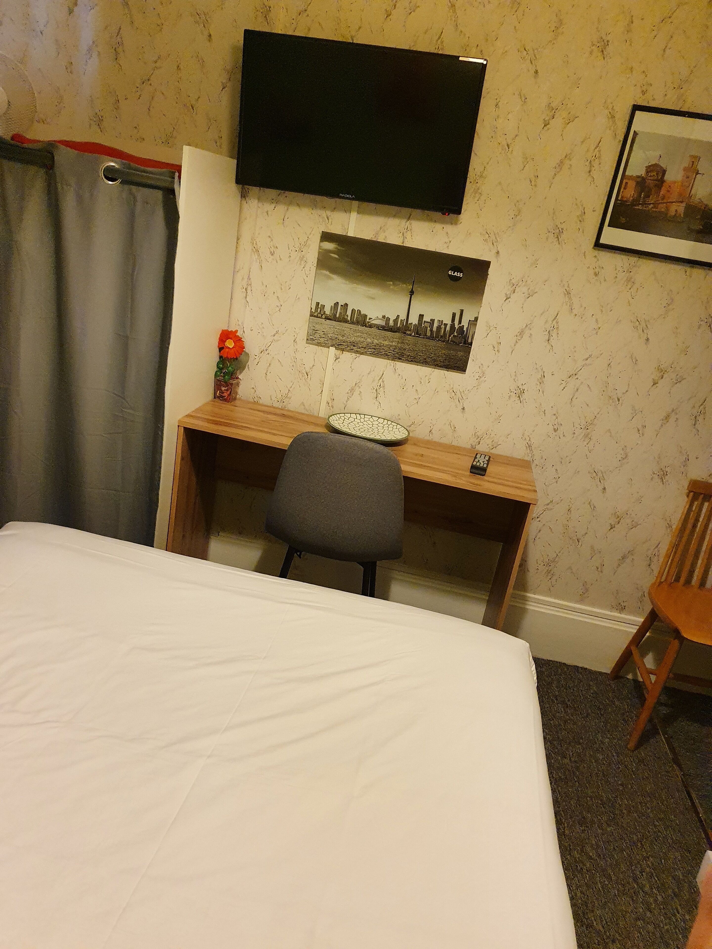 Une chambre d’hôtel comprenant un lit, un bureau avec une chaise, un téléviseur fixé au mur et un tableau représentant une vue sur la ville.