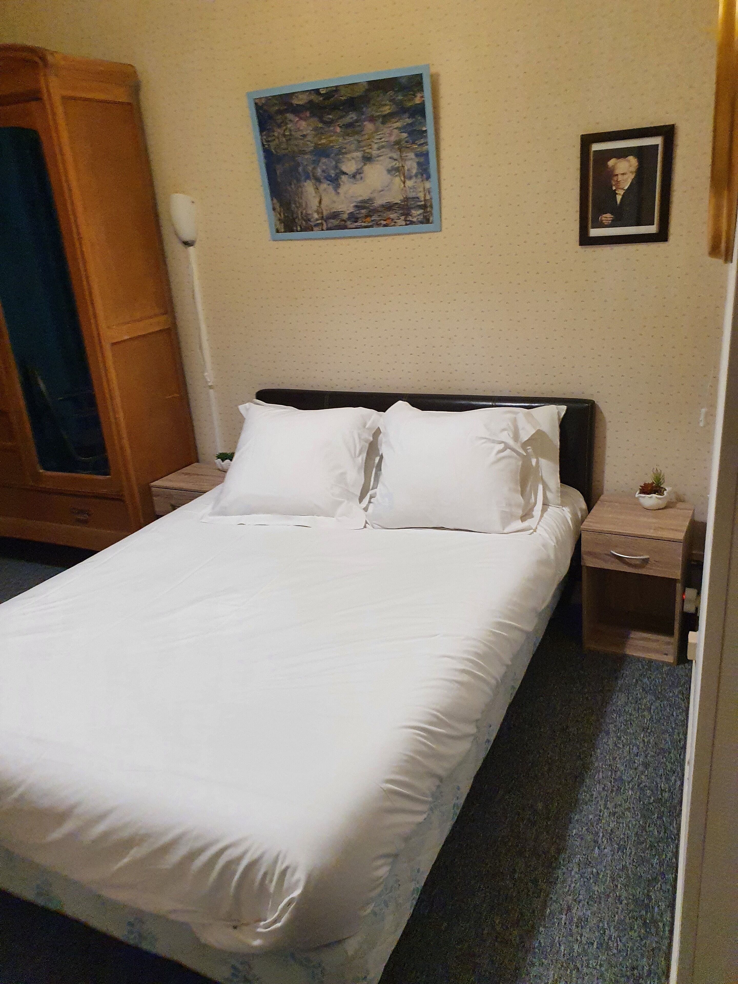 Una cama bien tendida con sábanas blancas, cabecera de madera y una mesita de noche con lámpara.