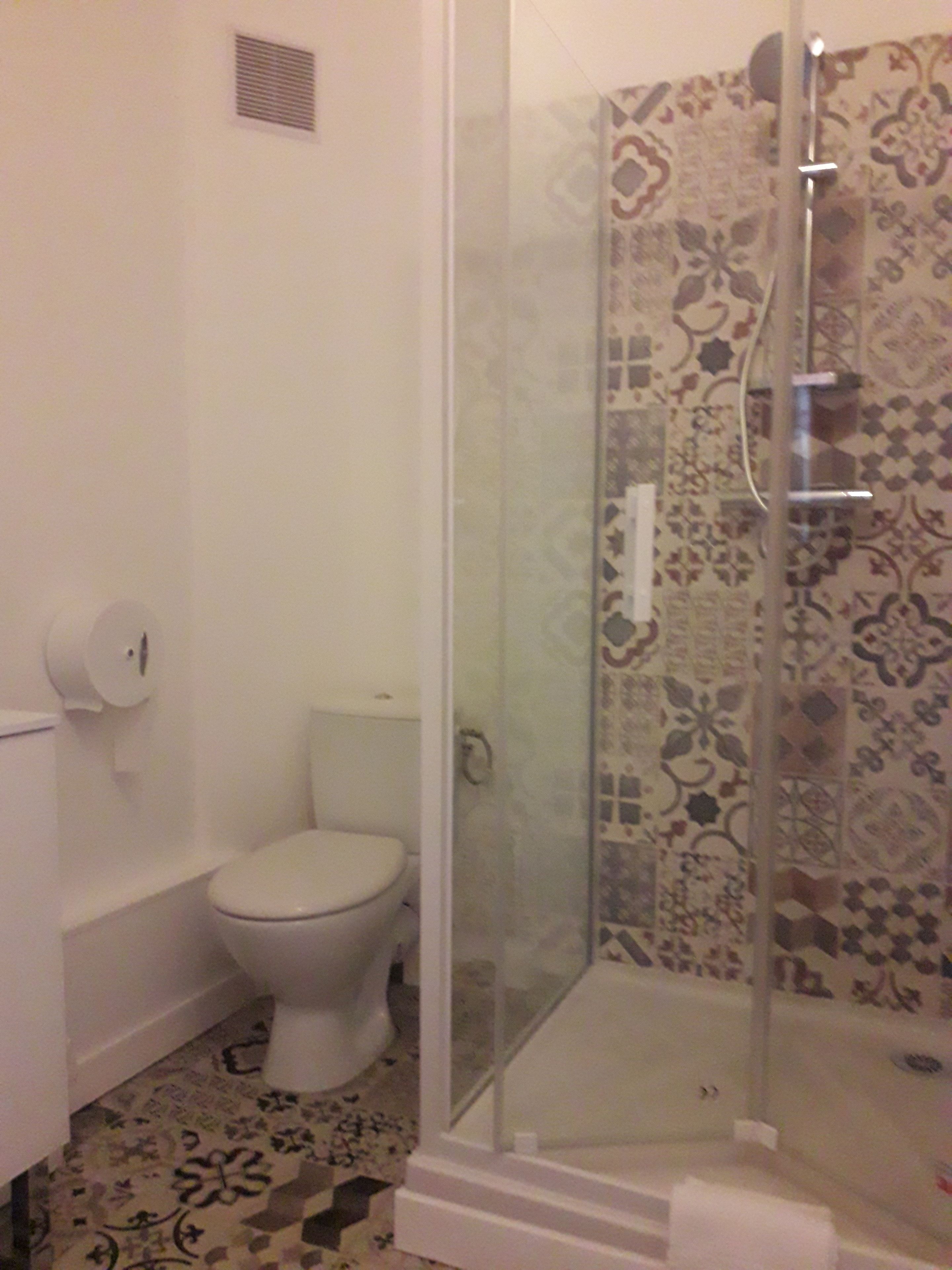 A bathroom with a toilet, a shower with a glass door, and patterned tiles on the walls.