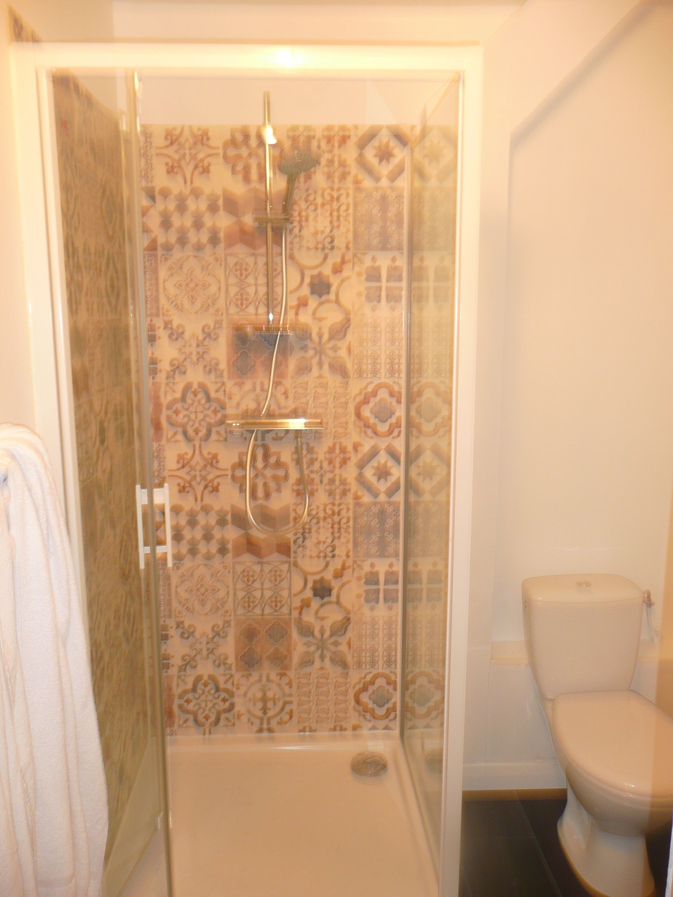 Een badkamer met douchecabine, toilet en betegelde wanden.