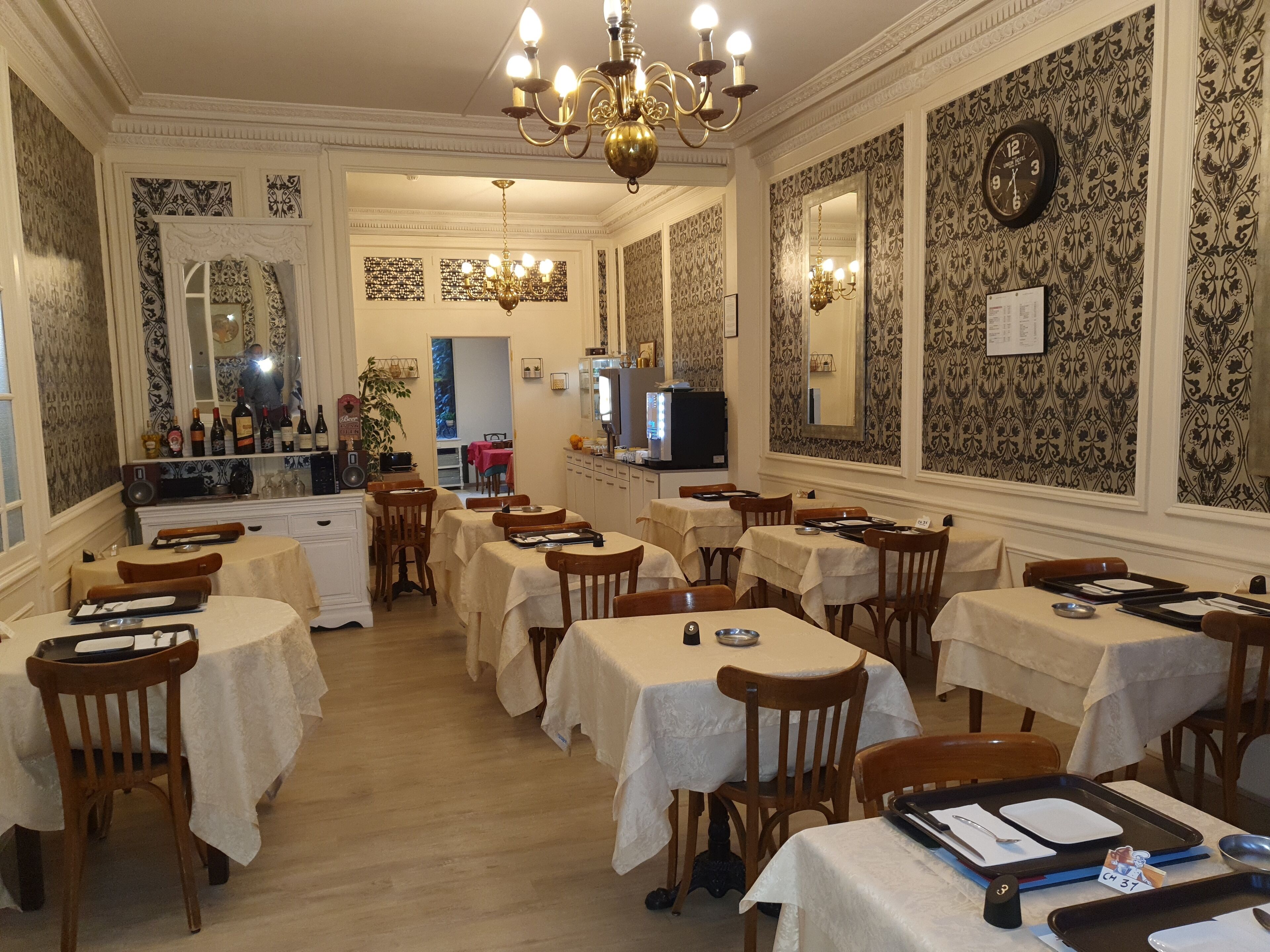 A dining area with multiple tables and chairs, a chandelier, and a clock on the wall.