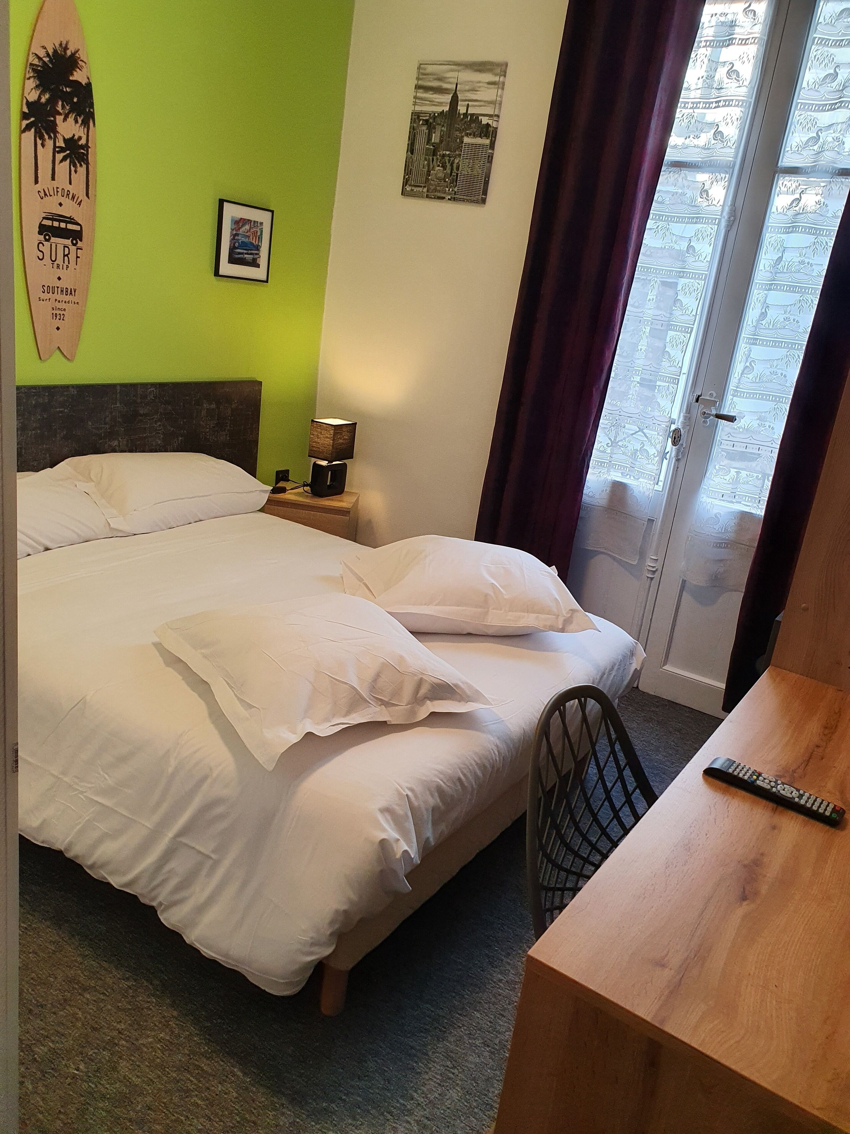 A hotel room with a bed, a nightstand with a lamp, a framed picture, and a surfboard decoration.