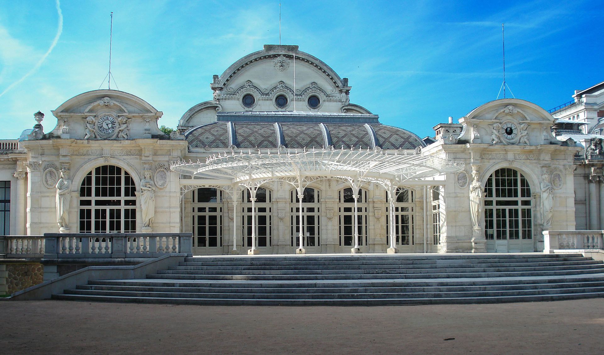 A grand building with a large central dome, arched windows, and a covered entrance area.