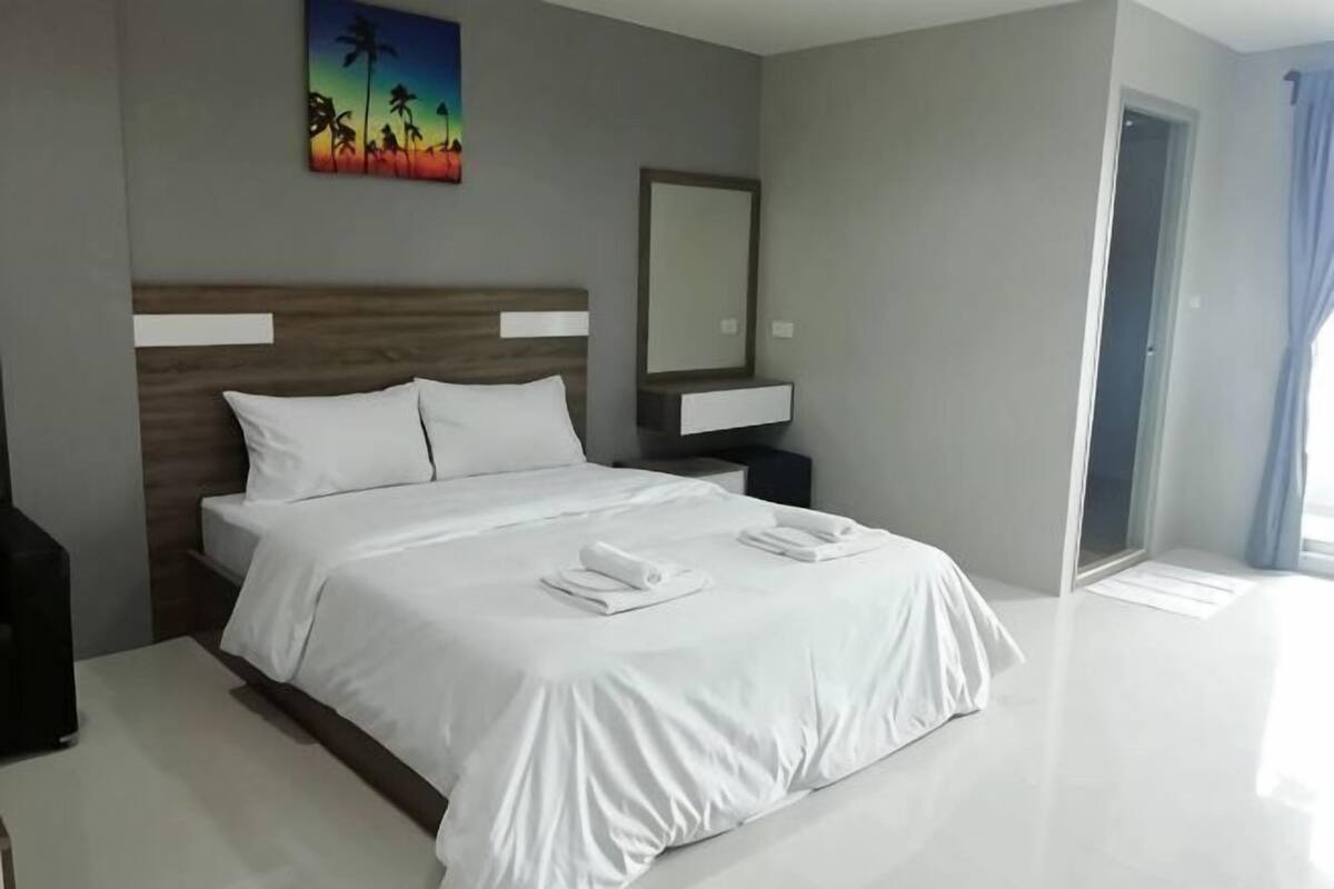 A modern hotel room with a large bed, a nightstand, a mirror, and a painting on the wall.