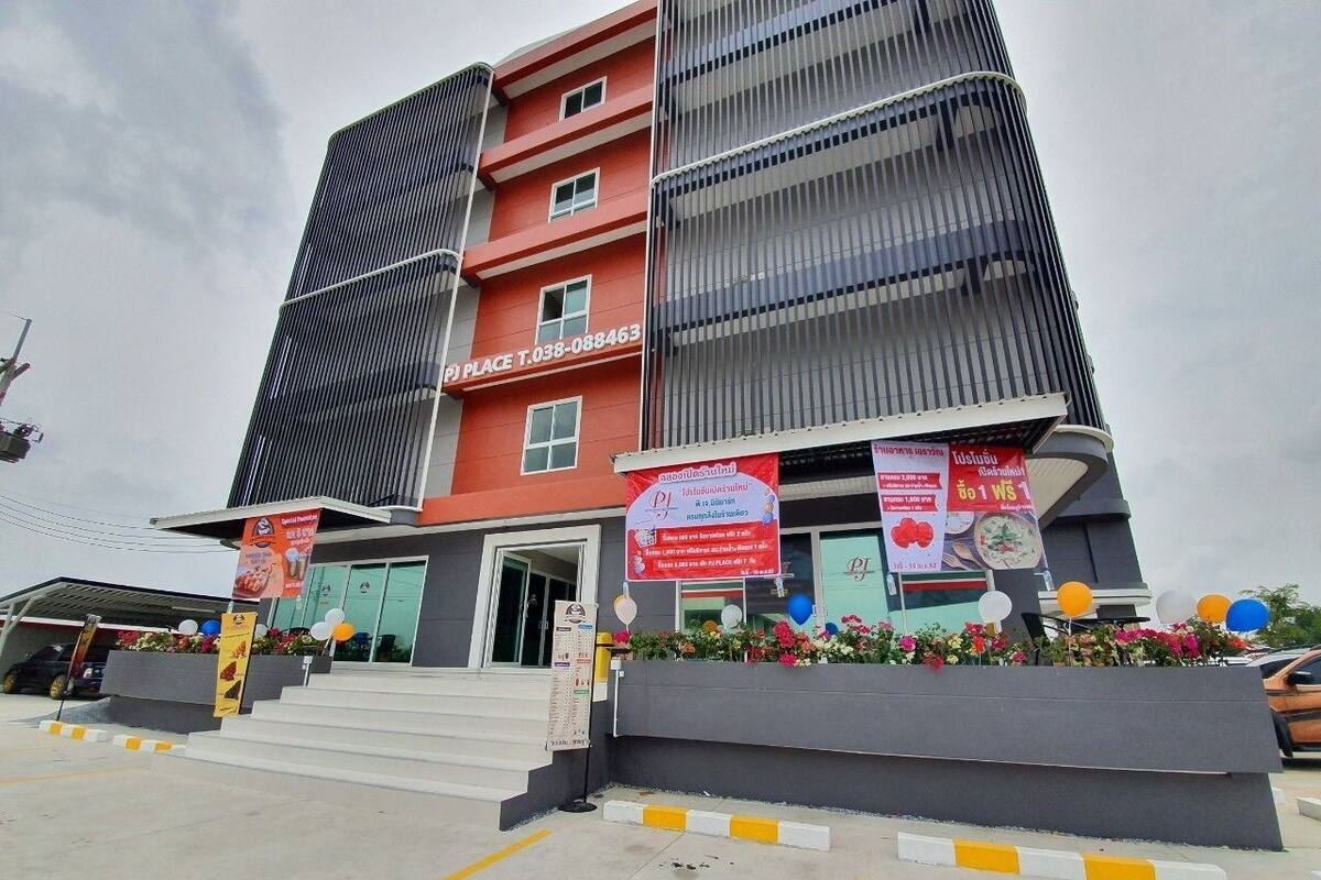 A multi-story building with a red and grey facade, a visible entrance, and a signboard with text.