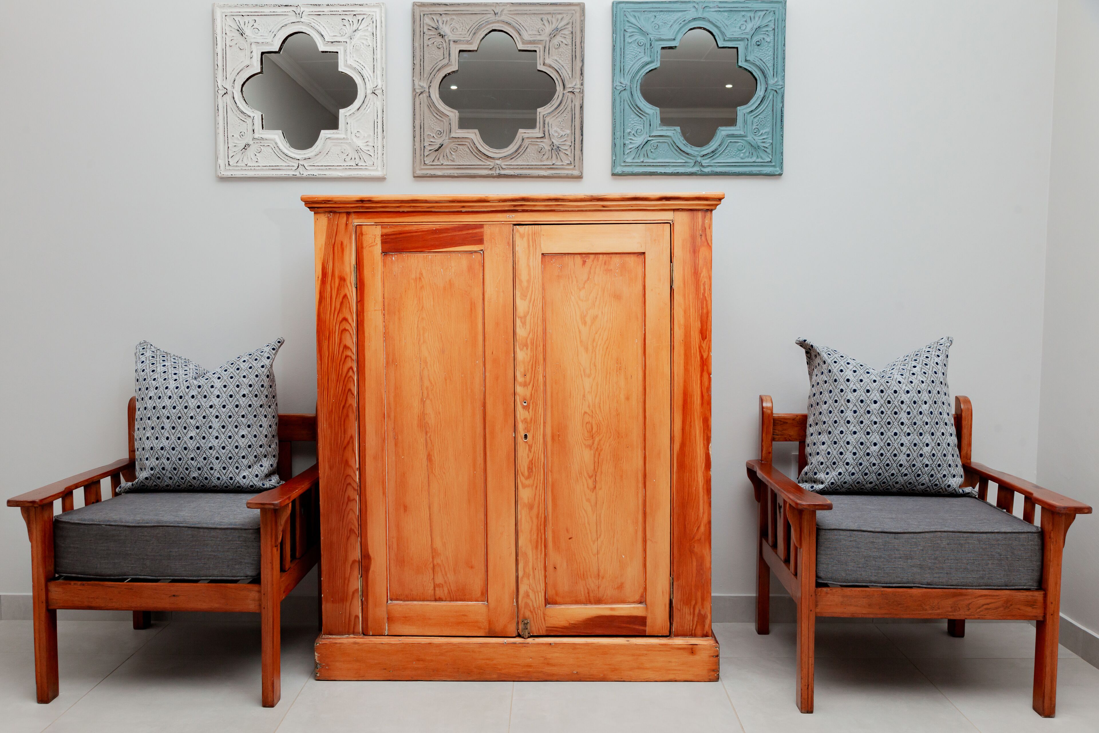 Une armoire en bois, accompagnée de deux chaises assorties, chacune dotée d’un coussin à motifs.