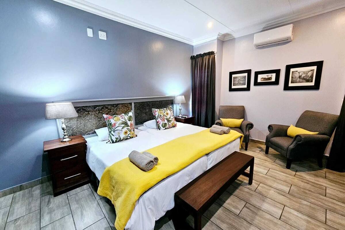 A hotel room with a bed, a bench, a chair, a nightstand, and a wall-mounted air conditioner.