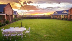 A spacious outdoor area with a lawn and a round table with chairs, surrounded by brick buildings. - 2 Owls Guesthouse (Potchefstroom)