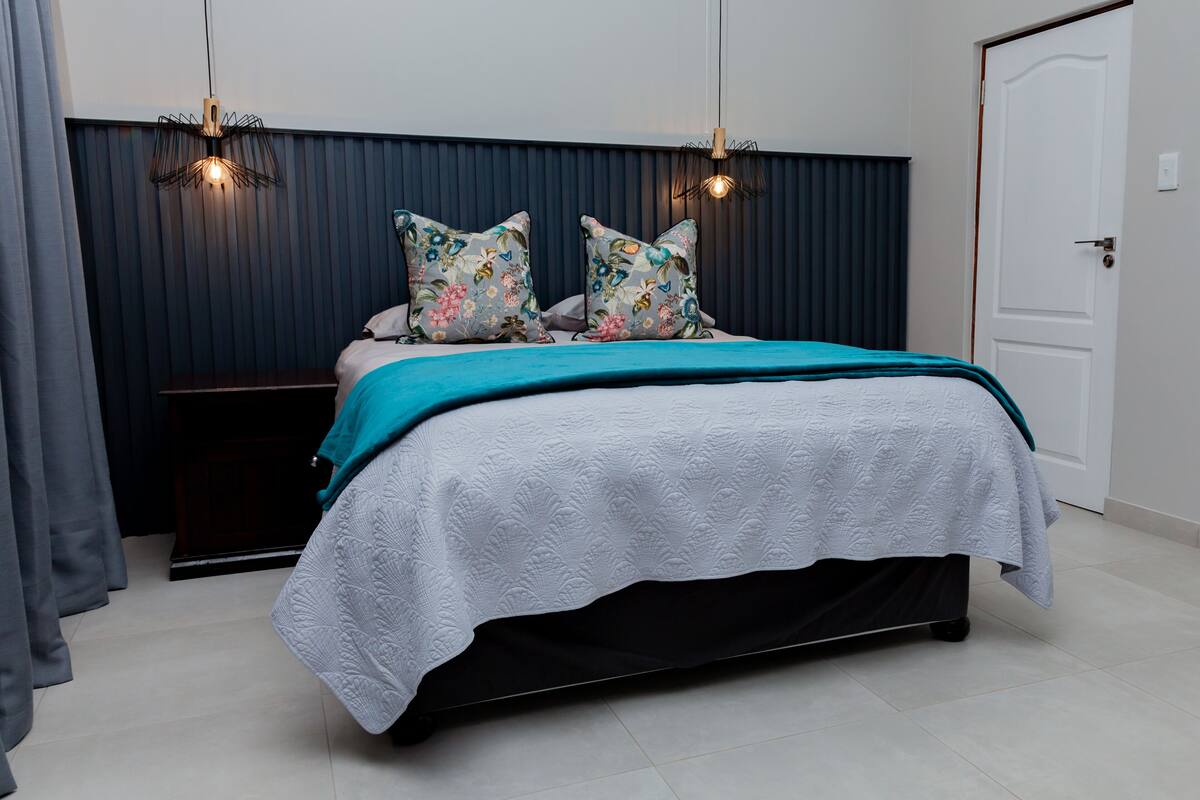 A bedroom with a bed, two wall-mounted lights, a door, and a dark-colored headboard.