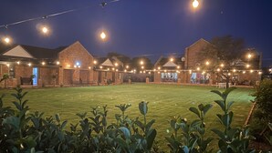 A courtyard with a lawn, surrounded by brick buildings with string lights. - 2 Owls Guesthouse (Potchefstroom)