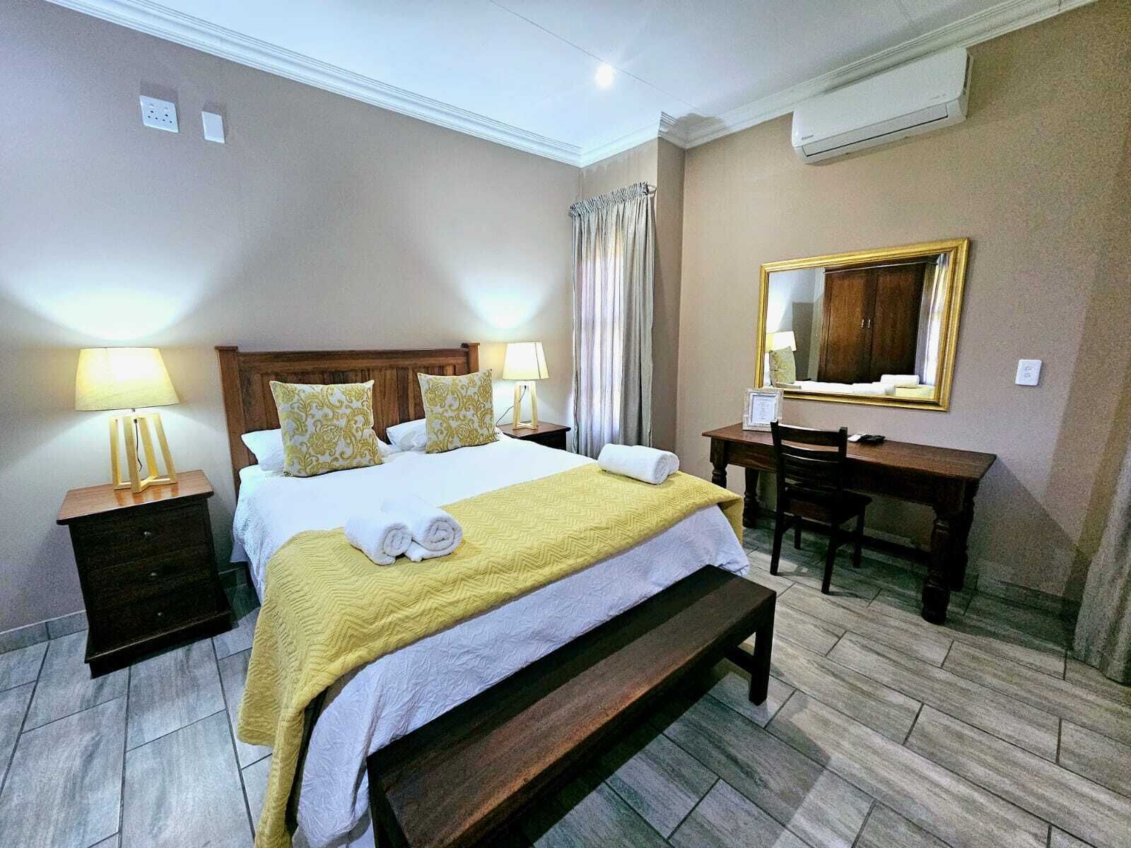Une chambre d’hôtel comprenant un lit, des tables de chevet, un bureau, une chaise, un banc, un miroir et un appareil de climatisation.