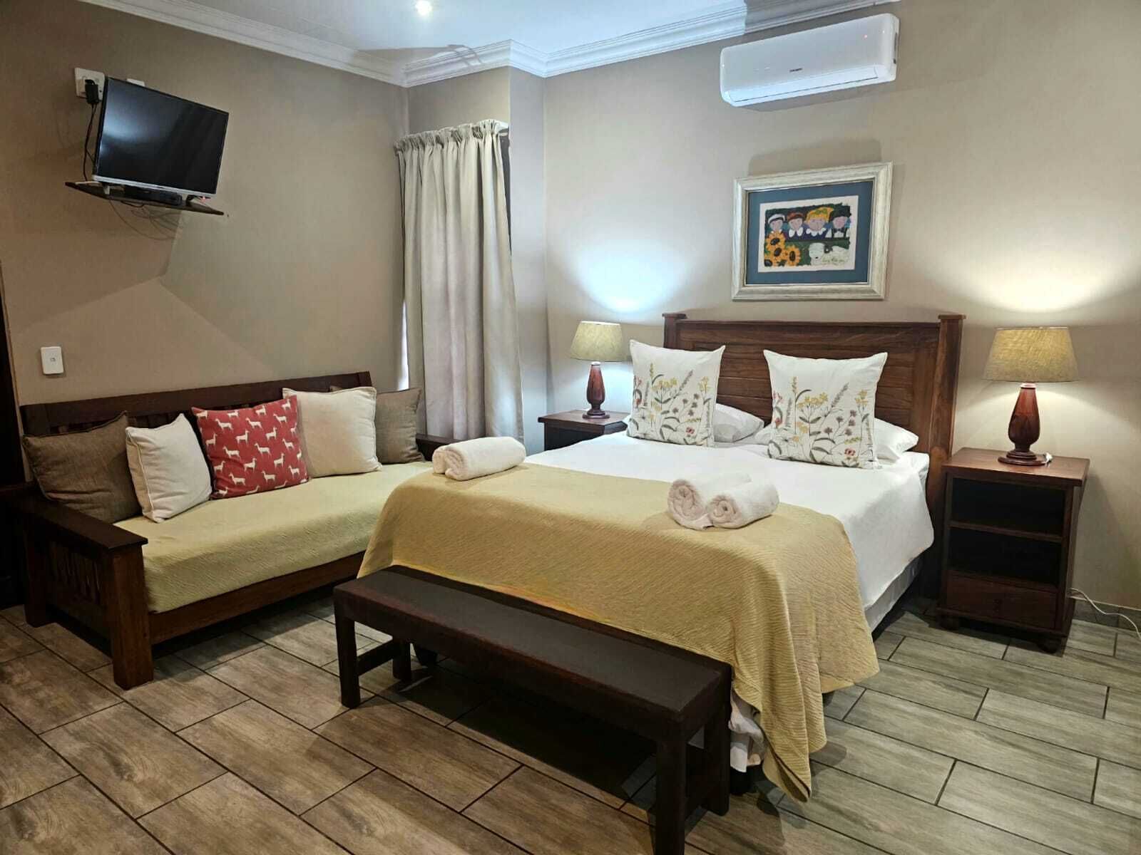 Quarto de hotel com duas camas, uma televisão presa à parede, um quadro na parede e um banco de madeira.