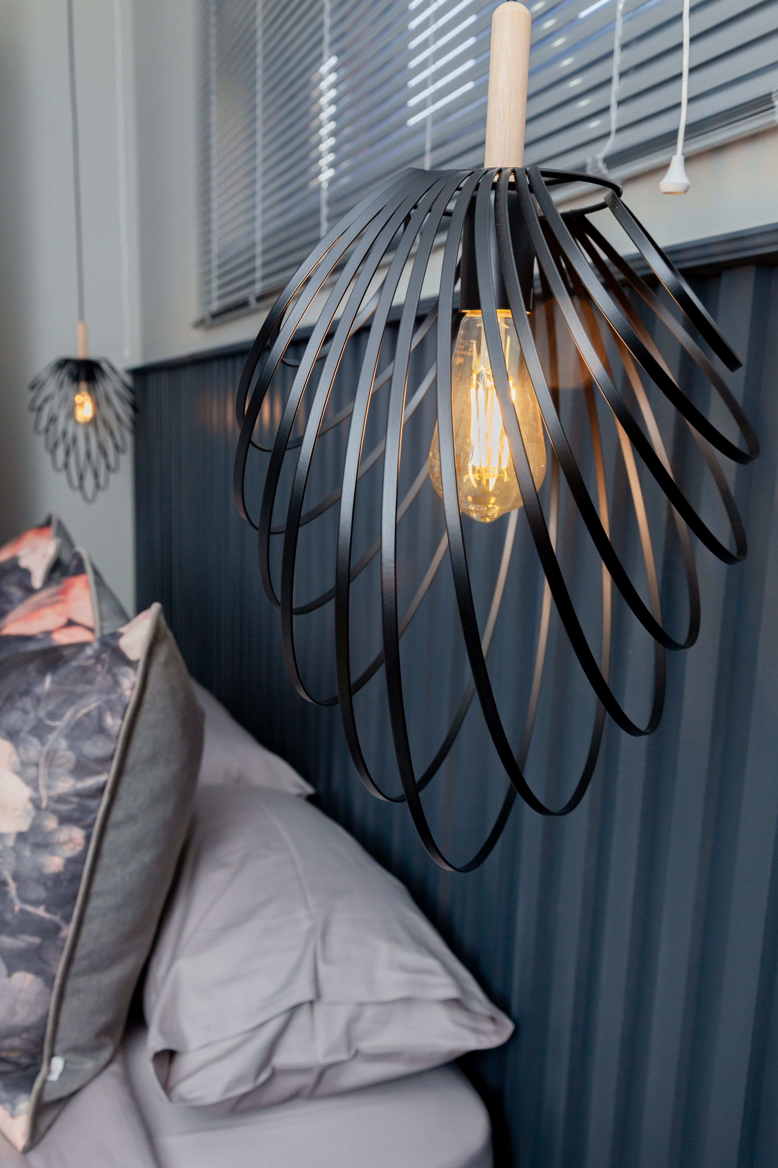 Una habitación moderna con una lámpara colgante de metal con un diseño original sobre la cama.