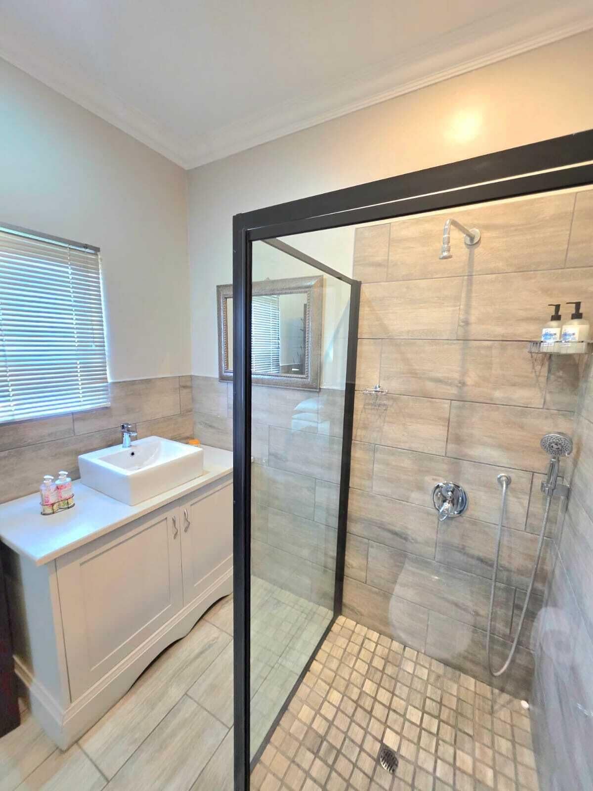 A modern bathroom with a glass-enclosed shower, a white vanity, and a window with blinds.