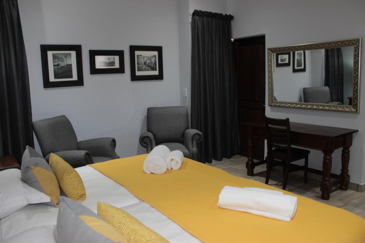 Ein Hotelzimmer mit einem großen Bett, zwei Sesseln, einem Schreibtisch und einem Spiegel.