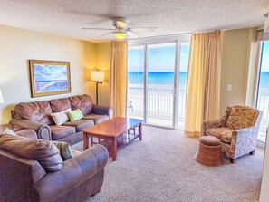 A living room with a sofa set, a coffee table, a patterned armchair, and a view of the ocean through large windows.