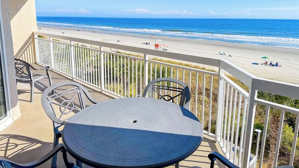 Un balcon avec une table et des chaises donnant sur une plage.