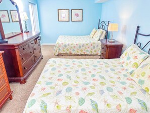 A bedroom with a large bed, a dresser, and a nightstand with a lamp.