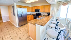 Eine Küche mit Holzschränken, einem Edelstahlkühlschrank, Granit Arbeitsplatten, einer Spüle und einer Frühstückstheke mit Hockern.