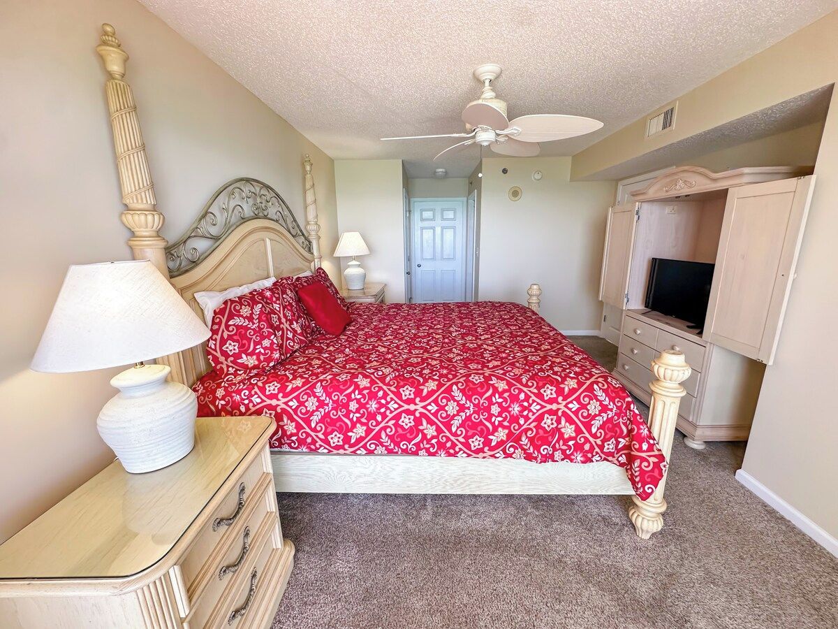 A bedroom with a bed, a nightstand, a dresser, a television, and a ceiling fan.