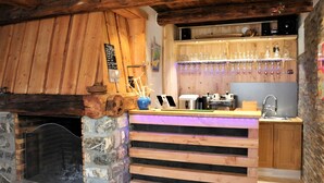 Eine rustikale Bar mit Kamin aus Stein, einer Holztresen und einer Vitrine für Gläser.