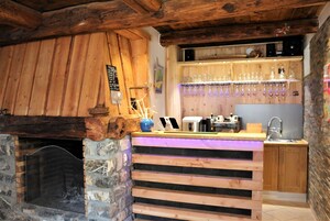 Un coin bar au style rustique, avec une cheminée en pierre, un comptoir en bois et une étag ère remplie de verres.