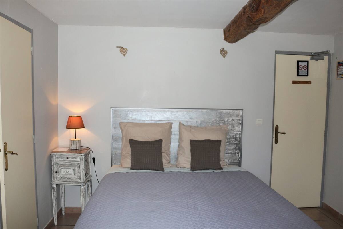 A bedroom with a bed, two pillows, a nightstand with a lamp, and a door with a sign.