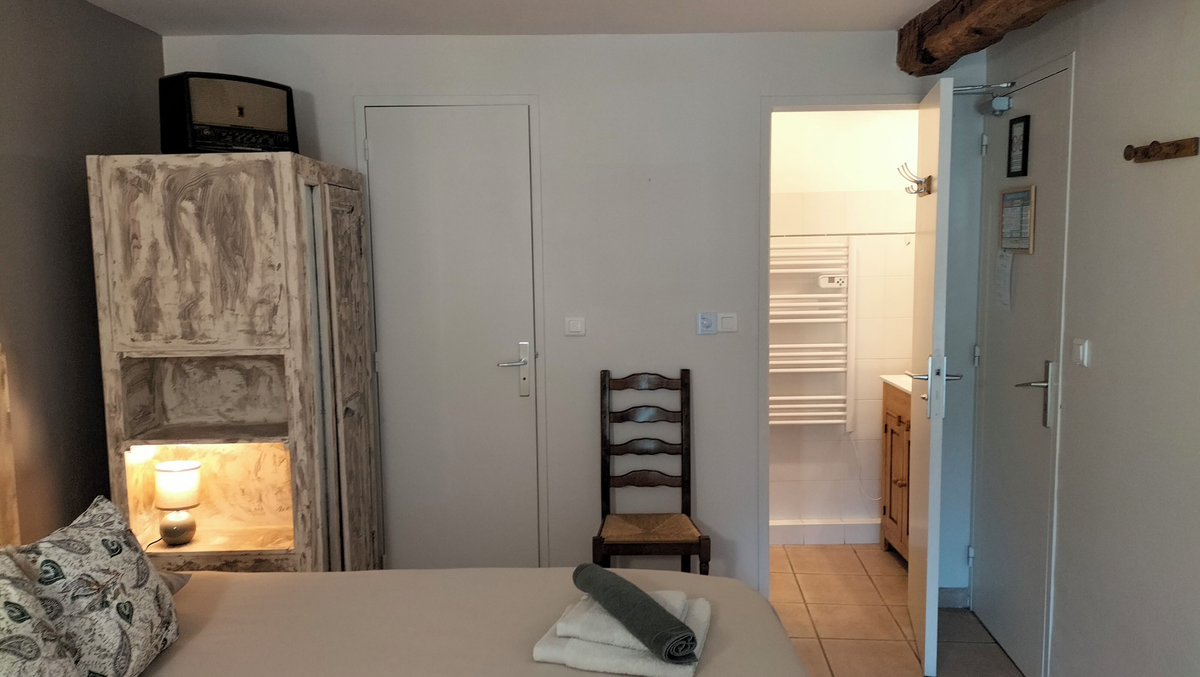 A bedroom with a bed, a chair, a wardrobe, and a bathroom visible through an open door.