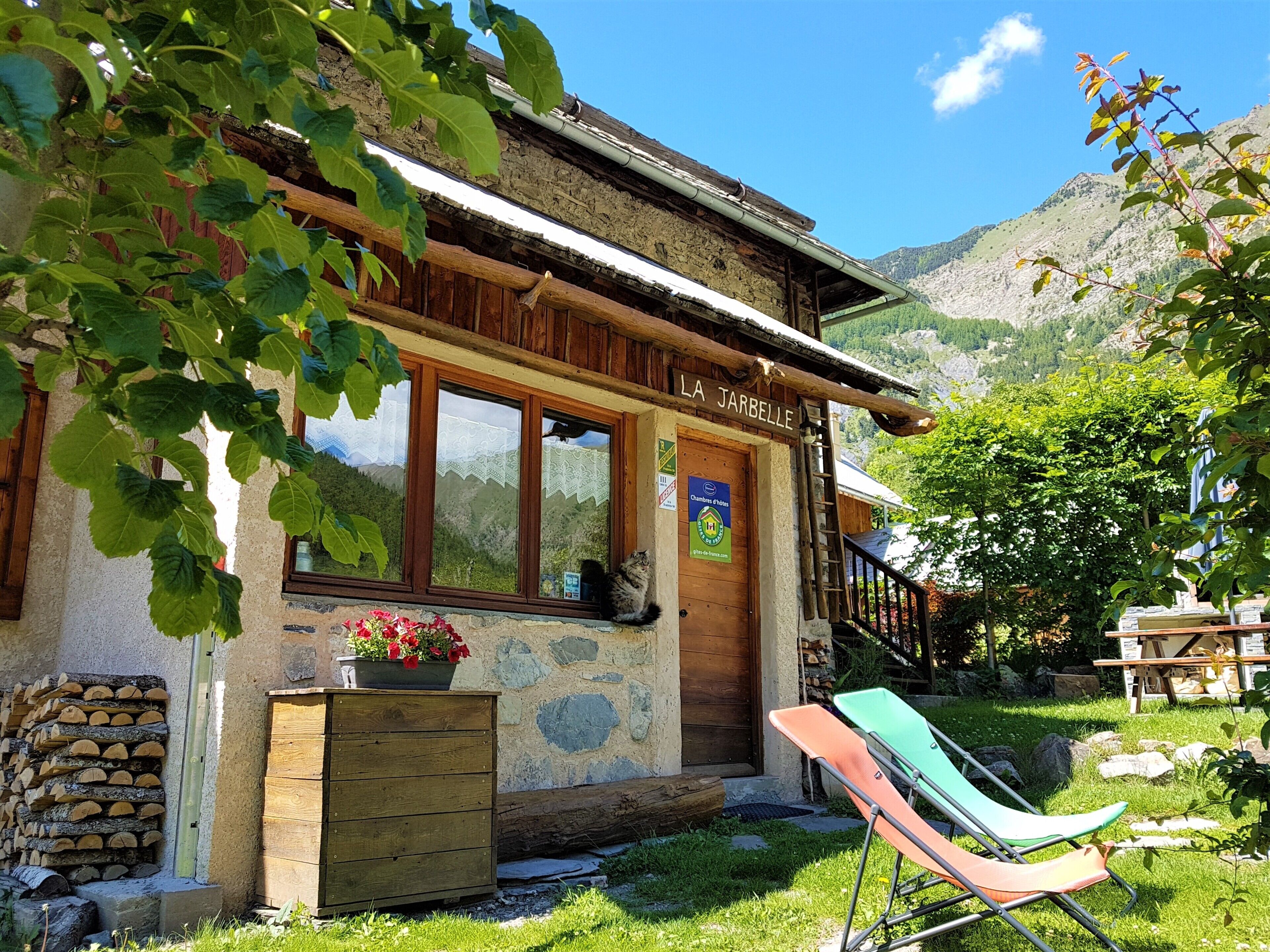 A rustic mountain lodge named "LA JARBELLE" with a stone facade, wooden shutters, and a wooden deck.