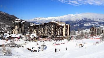 Une station de ski comprenant plusieurs bâtiments, dont un grand hôtel doté de balcons et une zone dédiée aux remontées mécaniques.
