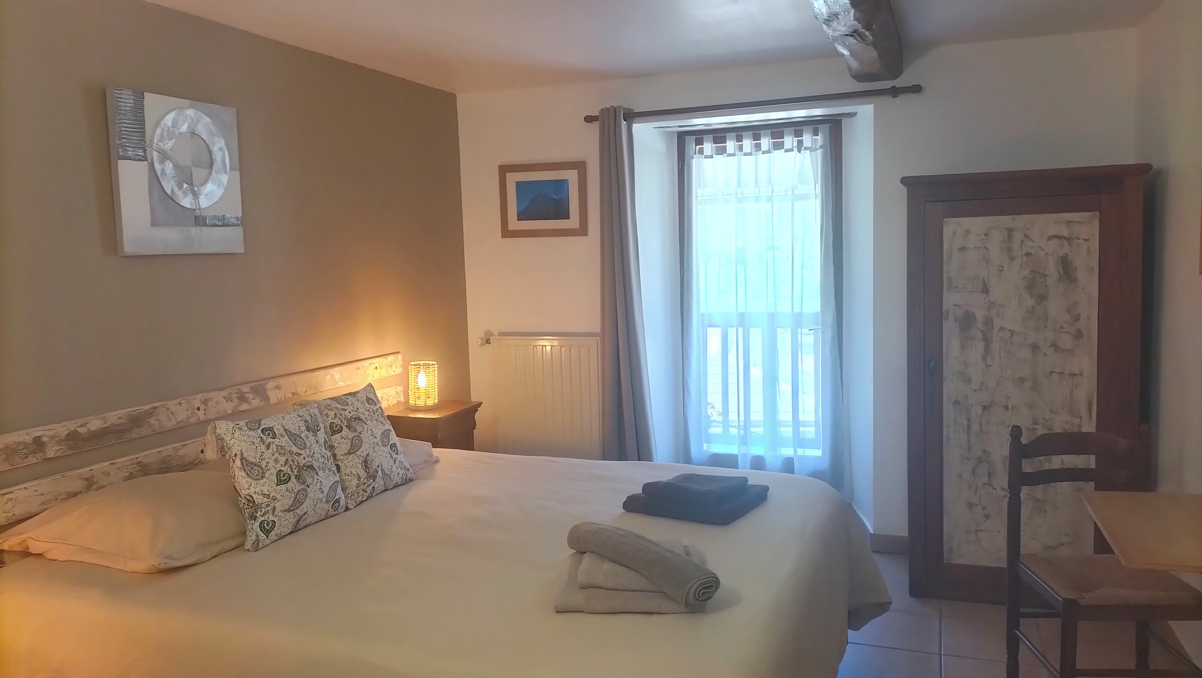 A hotel room with a bed, a nightstand, a lamp, a chair, a window with curtains, and a door.