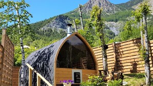 Eine Holzhütte mit geneigtem Dach, umgeben von einem Holzzaun, vor einer Berglandschaft.