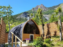 Une cabane en bois, dotée d’un toit en pente et entourée d’une clôture en bois, se dressant sur un fond de paysage montagneux.