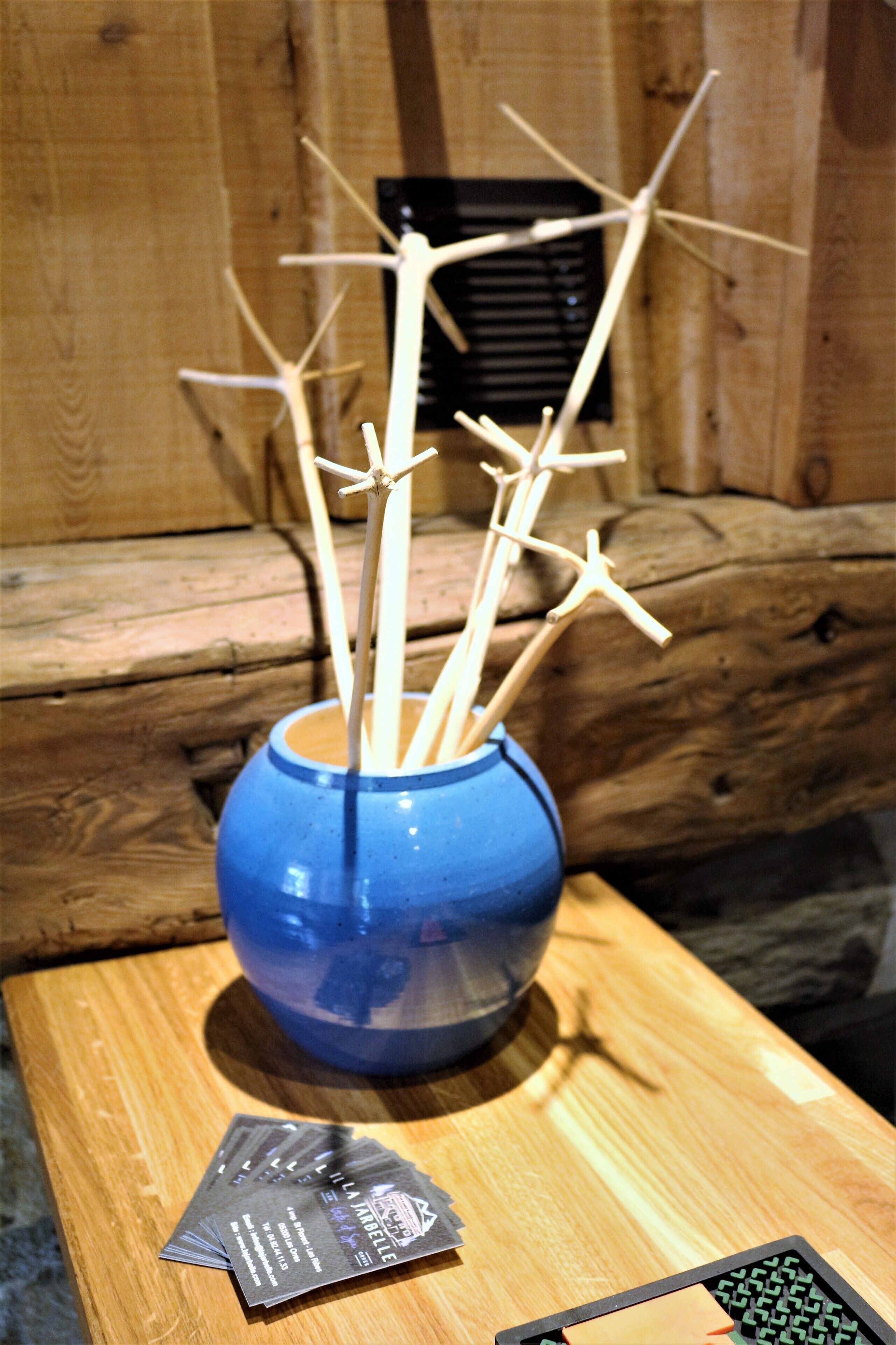 Un vase bleu avec des bâtonnets en bois, posé sur une table en bois.