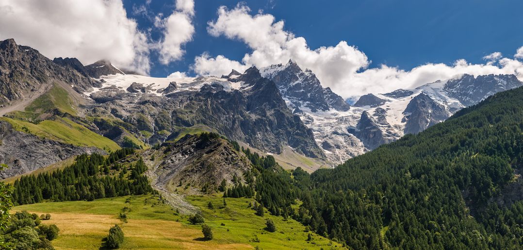 Un paisaje montañoso con cielo despejado, valles verdes exuberantes y picos nevados.
