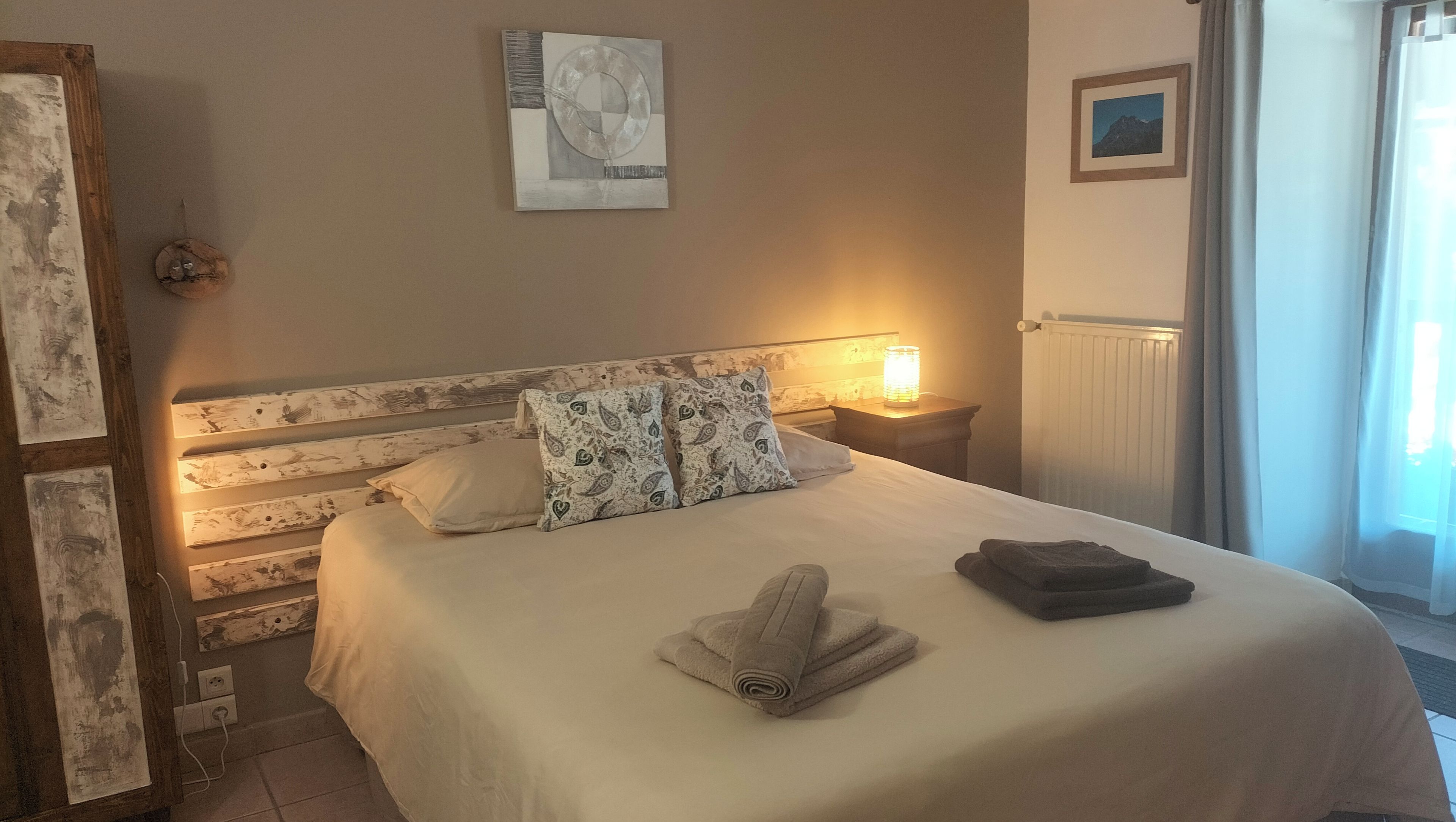A neatly made bed with a white duvet and patterned pillows, a bedside lamp, and a framed picture on the wall.