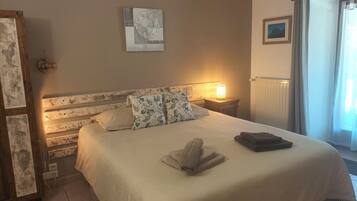 A neatly made bed with a white duvet and patterned pillows, a bedside lamp, and a framed picture on the wall.