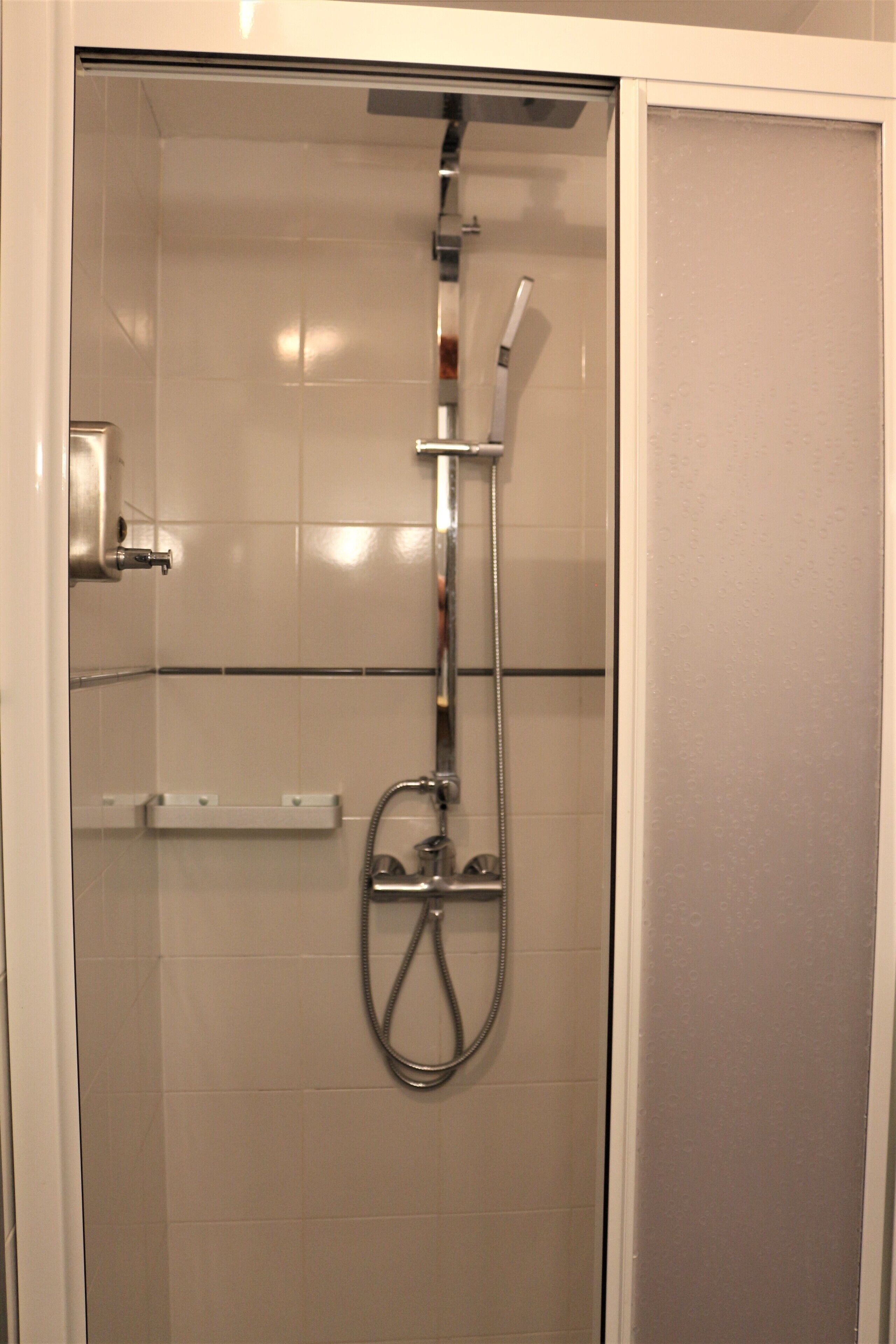 A glass-enclosed shower stall with a handheld showerhead and a wall-mounted faucet.