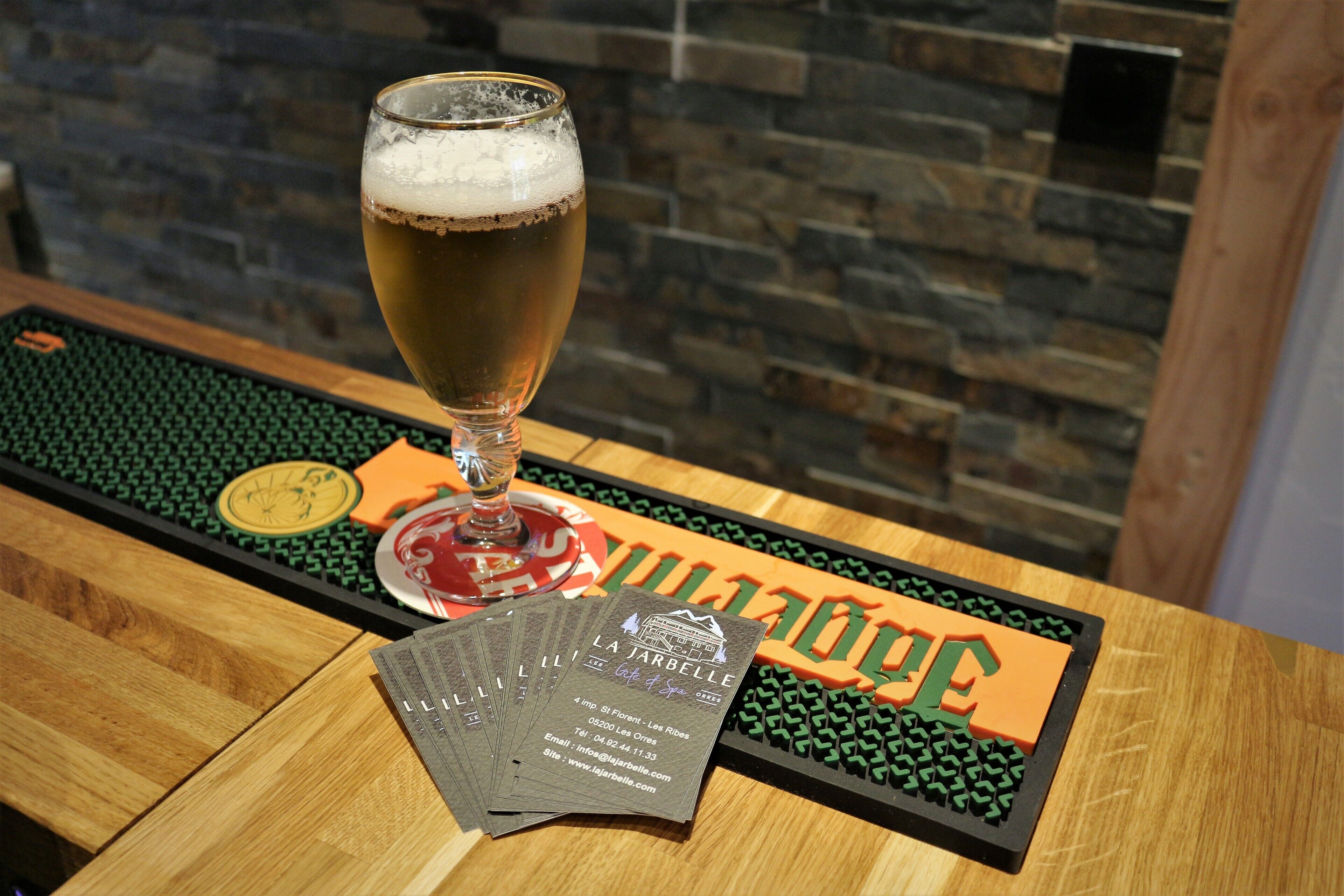 Una cerveza en un vaso sobre una mesa de madera con un posavasos y una tarjeta de presentación.