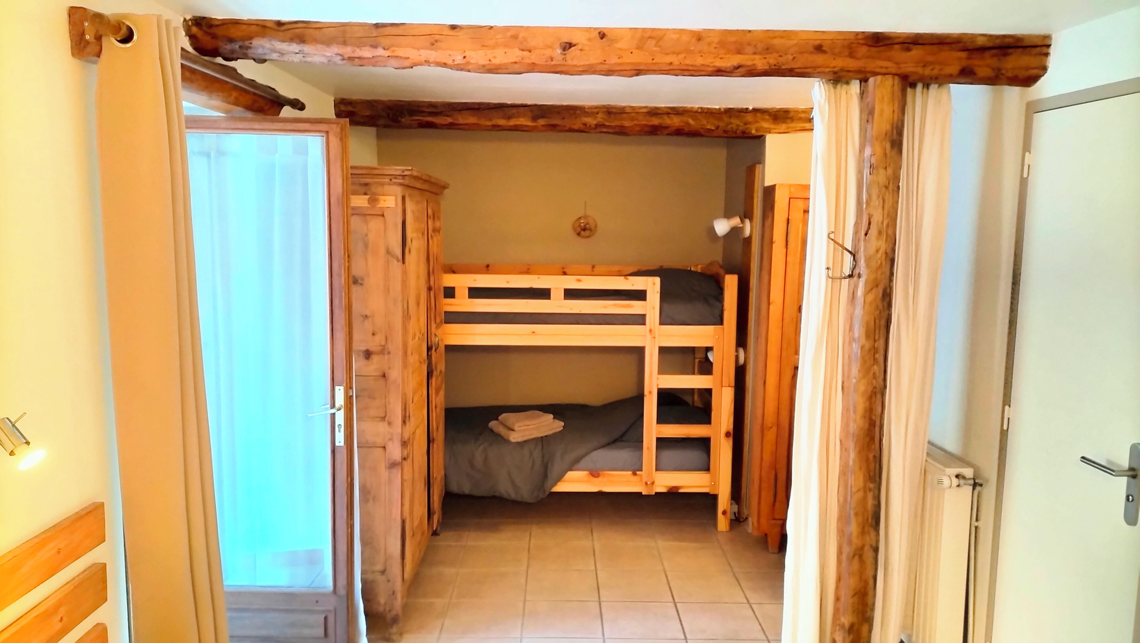 Une pièce avec un lit superposé, une armoire en bois et une porte donnant sur une autre pièce.