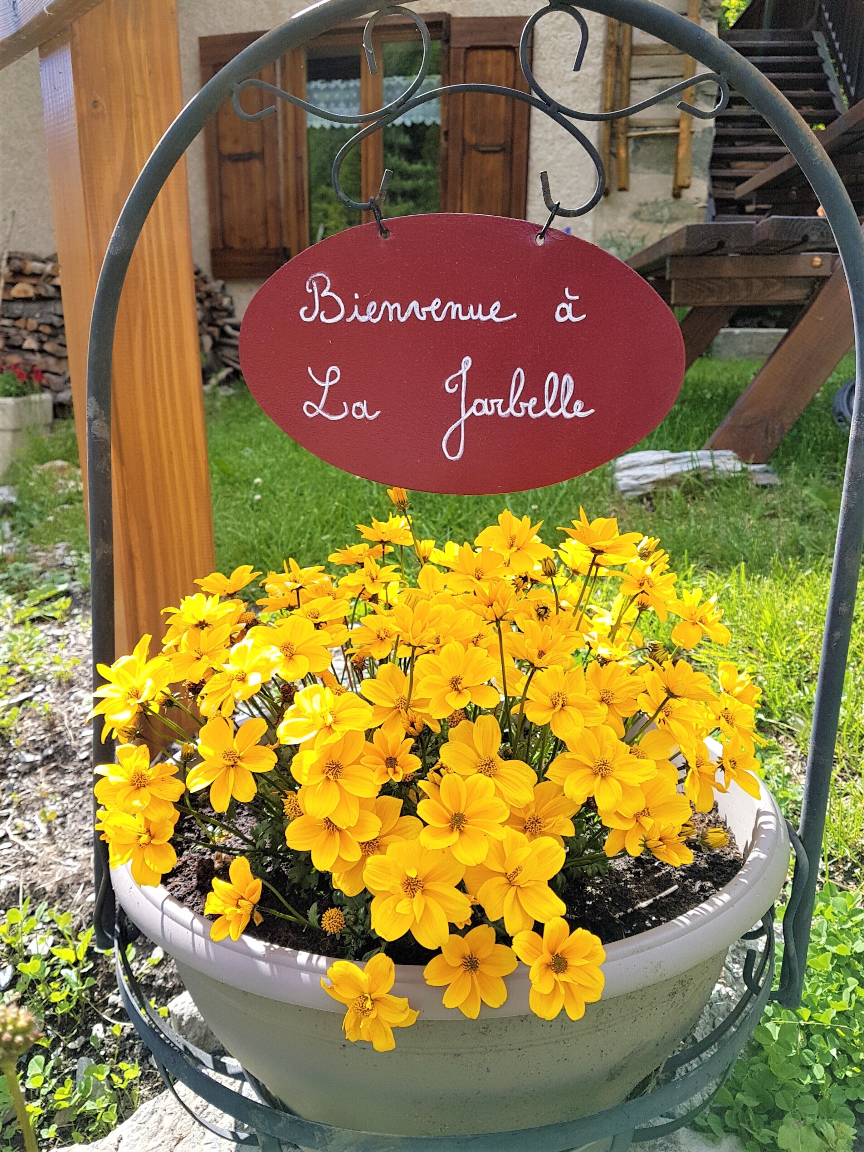Een bloemstuk met gele bloemen in een pot, met daarboven een bordje met de tekst 'Bienvenue à La Jarbelle'.